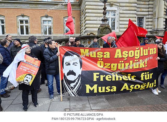 Protesters standing in front of the Criminal Justice Building holding red flags and banners with the text ""Freedom for Musa Asoglu!"" in Hamburg, Germany