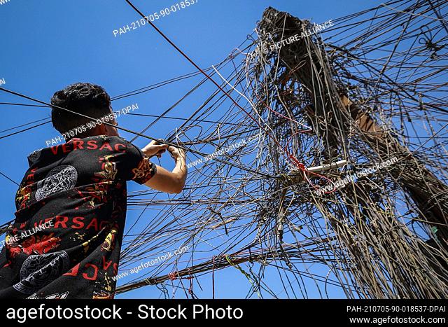 05 July 2021, Iraq, Baghdad: Ali Kazem, who owns a local private electricity generating station, connects cables to transfer electricity to homes