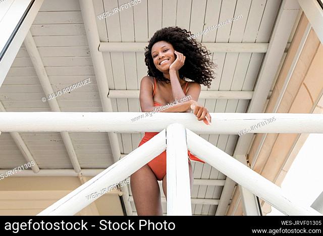 Smiling curly haired woman leaning on railing at lifeguard hut