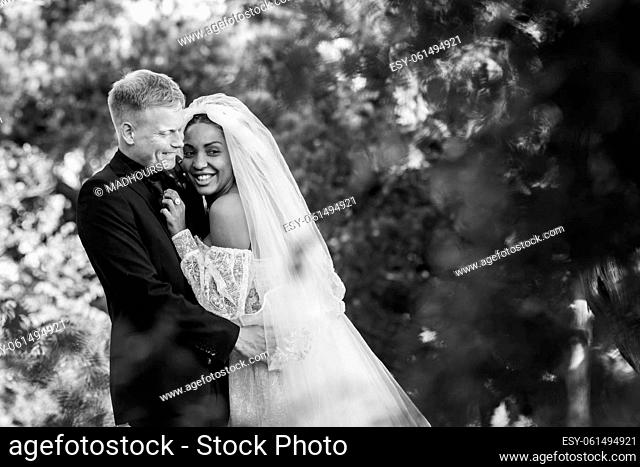 Portrait of interracial newlyweds hugging against the backdrop of a beautiful forest landscape, black and white photography