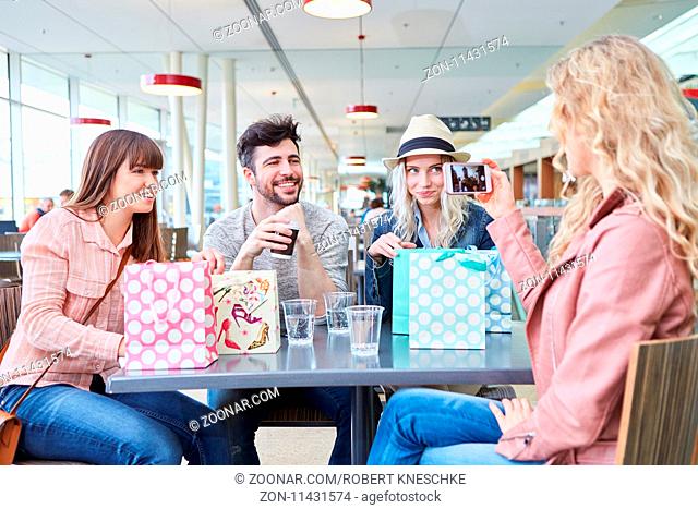 Frau fotografiert ihre Freunde mit dem Smartphone im Bistro nach dem Shopping