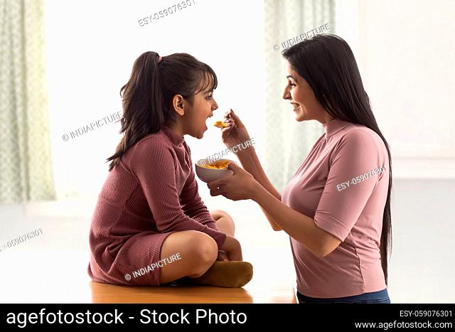 A HAPPY MOTHER GIVING CORNFLAKES TO DAUGHTER