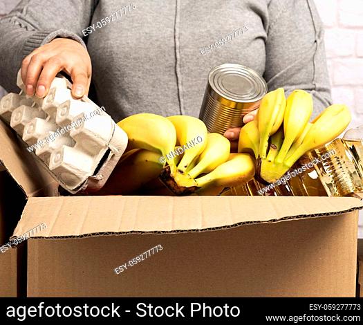 woman collects food, fruits and things in a cardboard box to help those in need, help and volunteering concept. Delivery of products