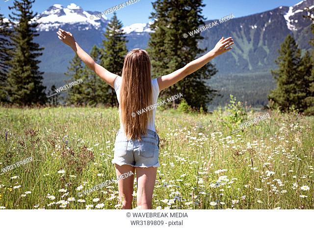 Girl spreading her arms in field surrounded by mountains on a sunny day