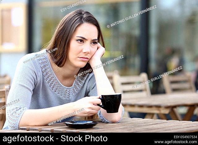 Sad young woman looking away holding a cup of coffee on a restaurant terrace