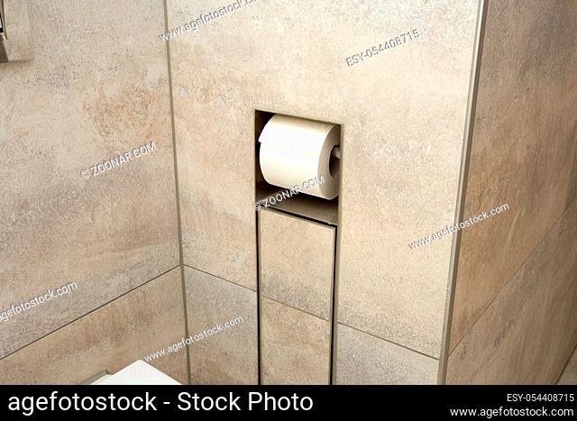 A white roll of soft toilet paper neatly hanging on a modern chrome holder in the wall close-up