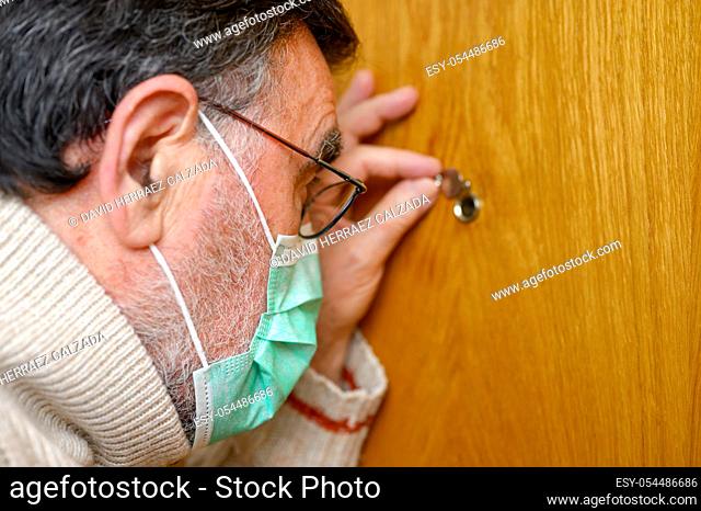 Covid-19 concept. Stay at home. Self-isolation to prevent the coronavirus pandemic. Senior man in protective green mask looks through the peephole
