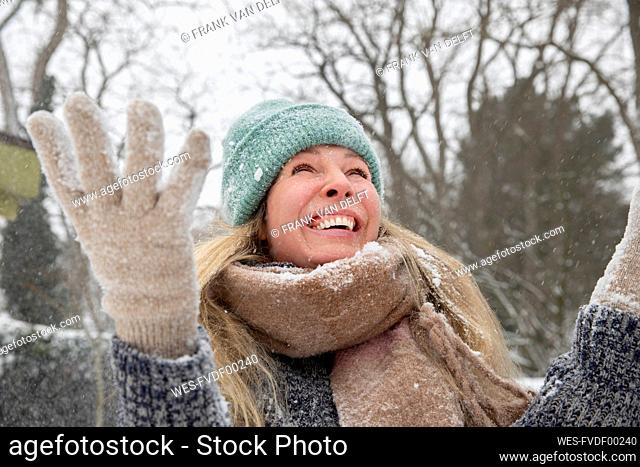 Cheerful blond woman throwing snowing while playing during winter