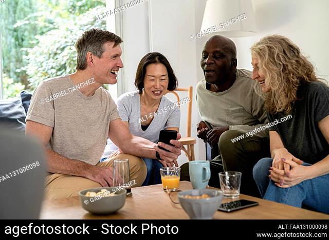 Senior couples gathered at living room while looking at smart phone