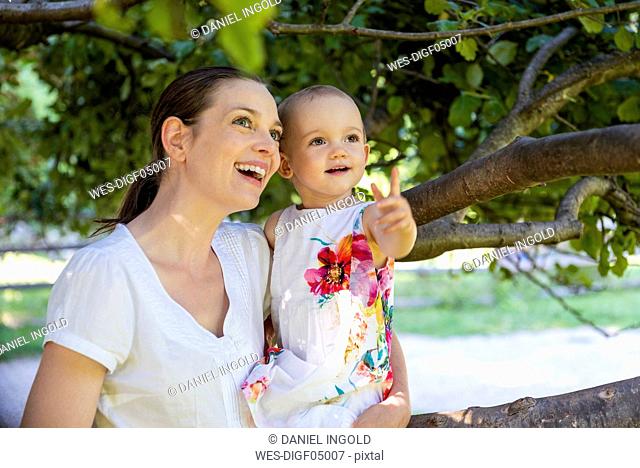 Happy mother and little daughter under a tree discovering something