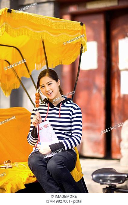 Young woman sitting on the rickshaw holding map and tomatoes on sticks