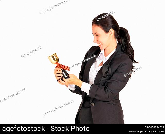 A businesswoman in a black suit with a smile looking at the trophy received from the work done proudly. Portrait on white background with studio light