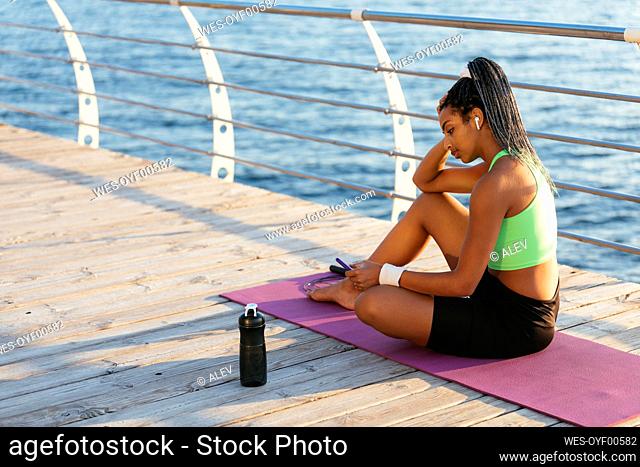Young woman using smart phone while sitting on exercise mat