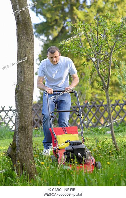 Germany, Kaufbeuren, Mid adult man gardening with lawn mower