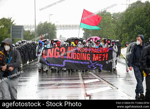 31 July 2021, Schleswig-Holstein, Brunsbüttel: Activists, accompanied by police, walk through ChemCoastPark with a placard reading ""LNG? Are you fracking...