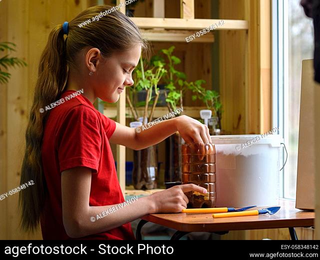 Girl pouring soil into a plastic bottle for planting seedlings of garden plants