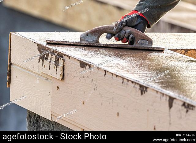 Construction worker using wood trowel on wet cement forming coping around new pool