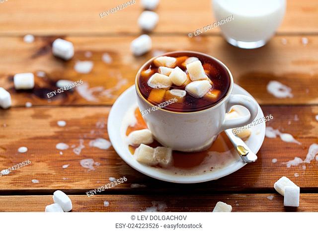 unhealthy eating, object and drinks concept - close up of lump sugar heap drowned in cup of coffee on wooden table