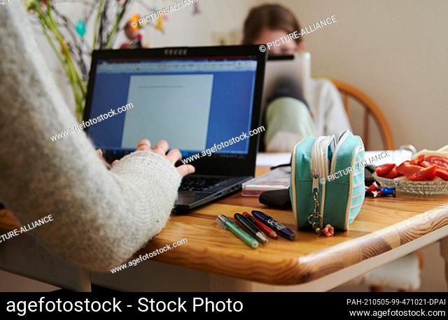 ILLUSTRATION - 29 April 2021, Berlin: A mother works at the kitchen table while her daughter looks into a tablet opposite