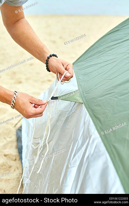 Young male tourist puts a green tent in the beach coast . The man sets up a camp on a hike, collects a tent alone, new normal travel