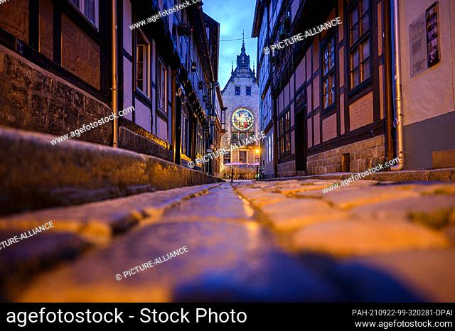 02 September 2021, Saxony-Anhalt, Quedlinburg: Evening view of the historic town hall through an alley of half-timbered houses in the old town of the Unesco...