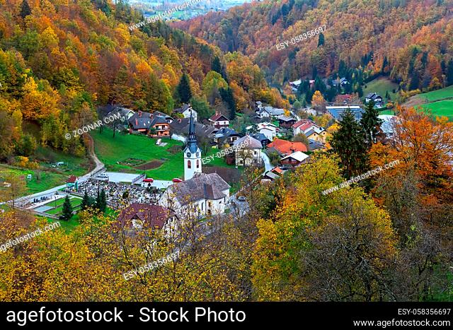 Mountain village slovenian countryside houses, church and autumn forest with colorful fall trees, Slovenia