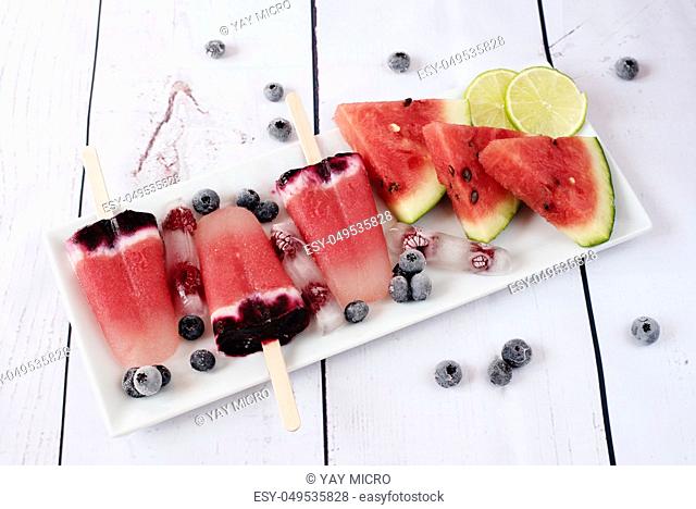 Popsicles with watermelon, coconut milk, lime, raspberries and blueberries. Popsicle on a white rectangular plateau, rectangle ice with raspberries