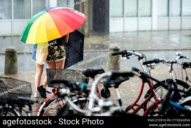 10 September 2021, Lower Saxony, Oldenburg: Two young women walk through downtown with a colorful umbrella during a thunderstorm