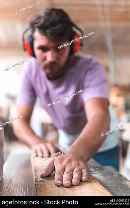 Male carpenter holding wooden plank in workshop