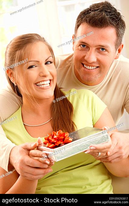Portrait of happy couple smiling at camera, cuddling and holding present