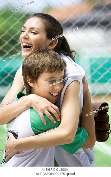 Young baseball player embracing his mother