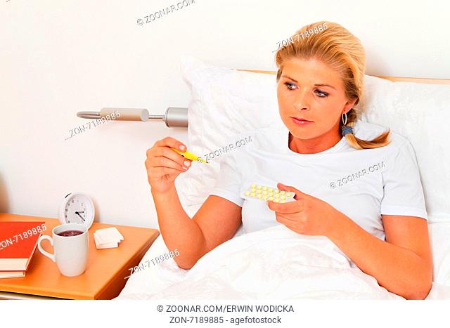 Eine Frau im Bett ist Krank und hat Fieberthermometer