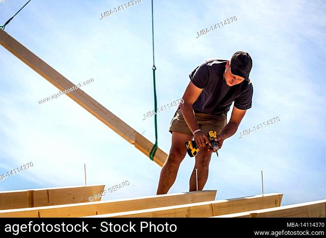 germany, bavaria, construction of a prefabricated wooden house, screwing roof beams with cordless screwdriver