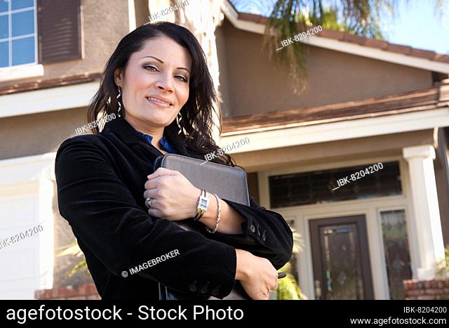 Proud, attractive hispanic real estate agent woman in front of new home