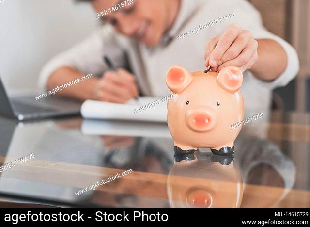 Man sit at desk manage expenses, calculate expenditures, pay bills online use laptop, makes household finances analysis, close up focus on pink piggy bank