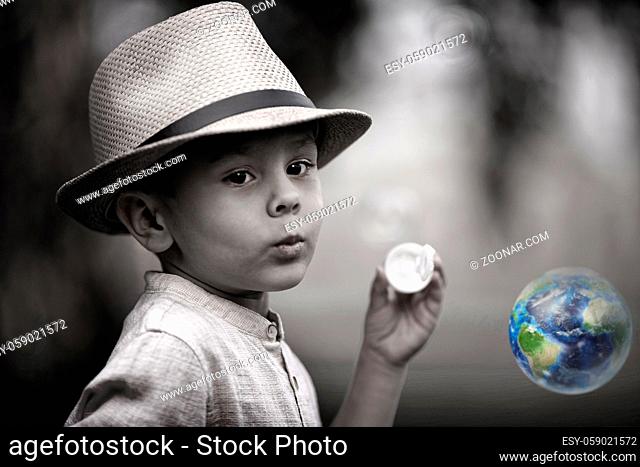 Conceptual portrait of a child. A little boy looks at a soap bubble in the shape of an earth. Hope for a colorful future. Monochrome image