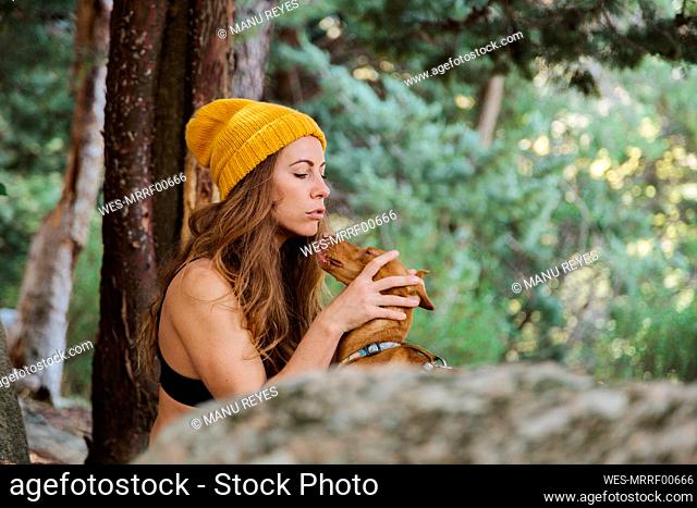 Mid adult woman playing with dog while sitting in forest at La Pedriza, Madrid, Spain