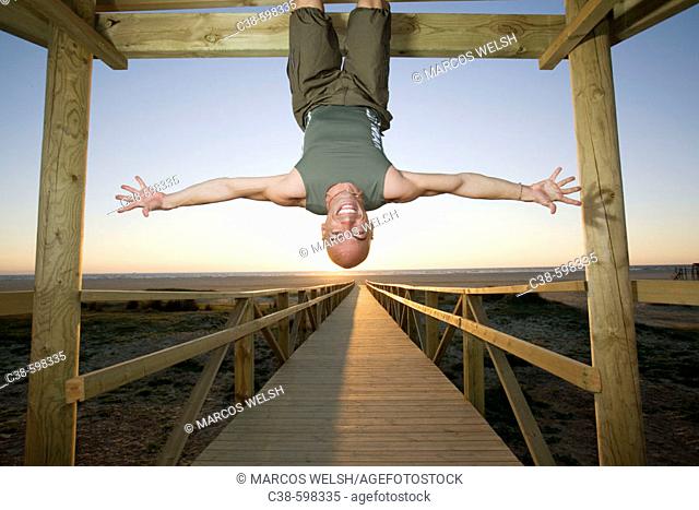 Man Hanging Up Side Down on Footbridge