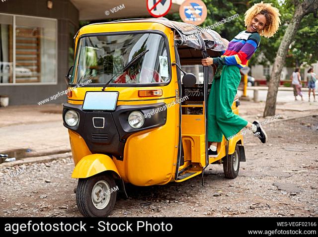 Cheerful young woman standing on rickshaw in city
