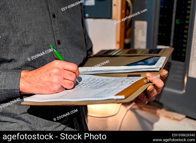 inspector holding a notebook in his hand next to an electric circuit breaker panel, Close up and selective focus of a man taking professional notes