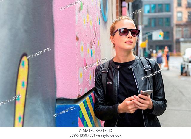 Closeup of female hipster with smart phone. Woman using smart phone app guite on city break weekend trip to East Village, New York city, USA