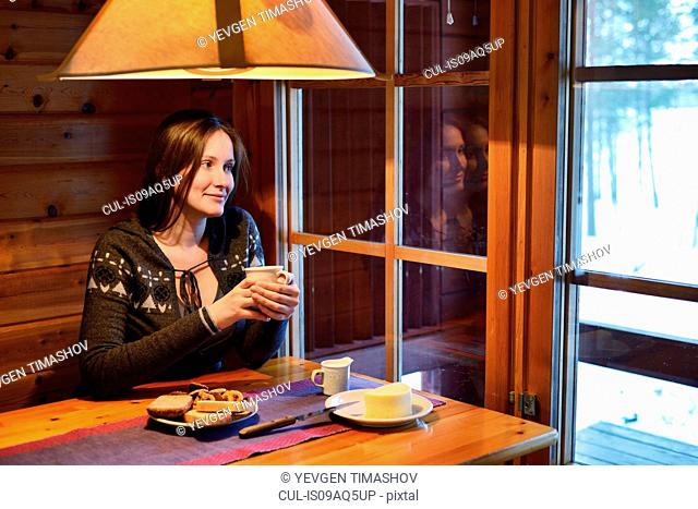 Portrait of young woman drinking coffee and looking out of window, Posio, Lapland, Finland