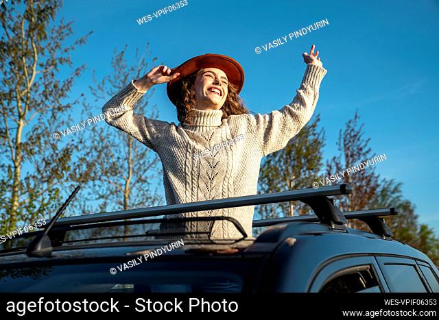 Cheerful woman wearing hat enjoying through sun roof of car