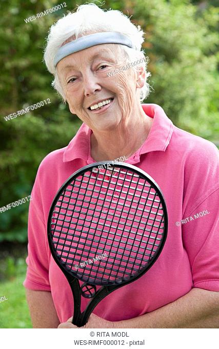 Germany, Bavaria, Huglfing, Senior woman holding badminton racket, smiling, portrait