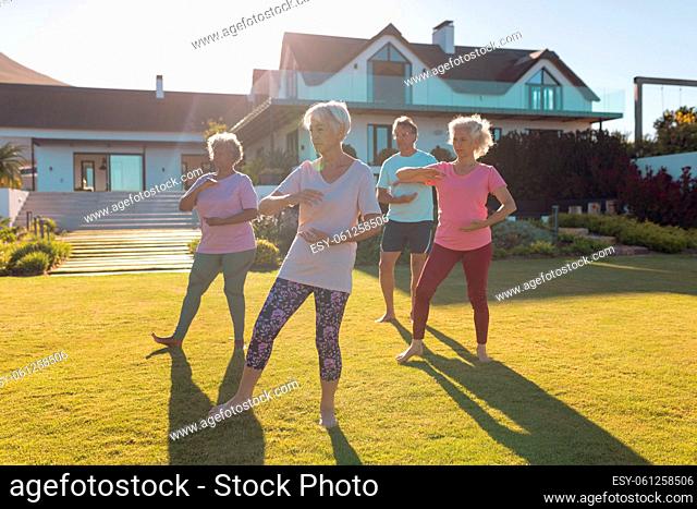 Multiracial male and female seniors exercising on grassy land in yard against retirement home