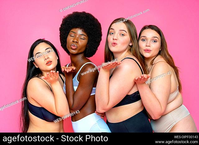 Multi-ethnic group of female models in lingerie blowing kisses against pink background