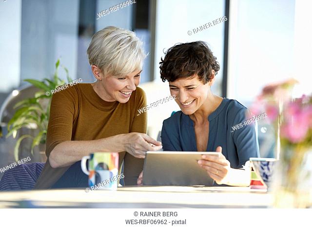 Two happy women sharing tablet at table