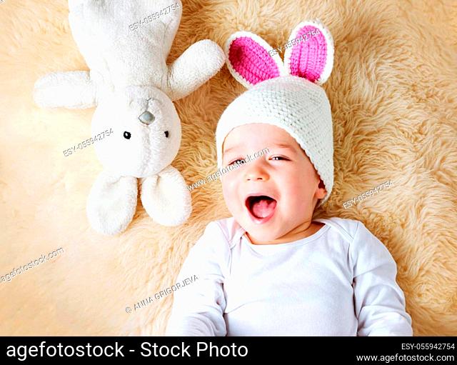 sleepy one year old baby lying in bunny hat on lamb wool background