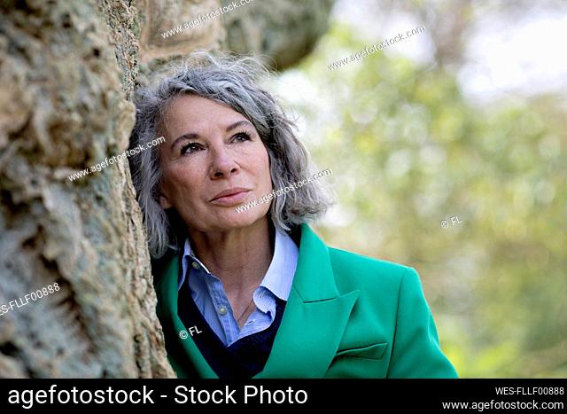 Contemplative senior woman leaning on tree