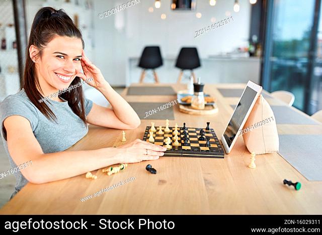 Lächelnde junge Frau spielt Schach im Videochat online zu Hause am Tablet Computer